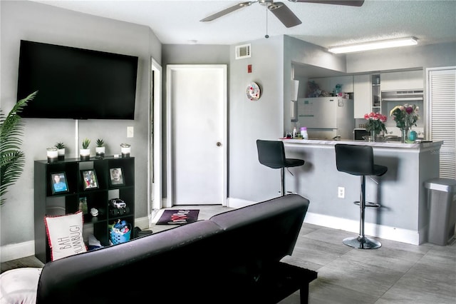 living area with baseboards, a textured ceiling, visible vents, and a ceiling fan