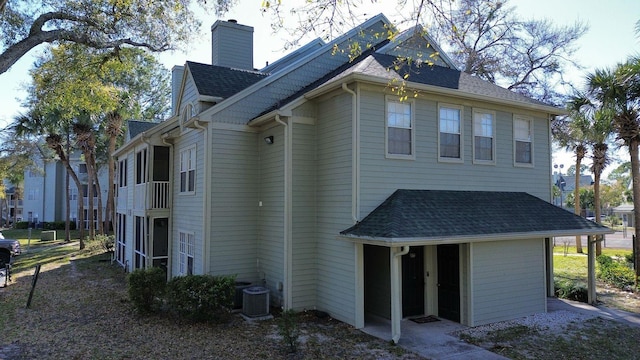 back of house featuring central AC, a chimney, and a shingled roof