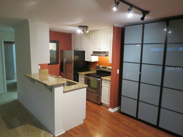 kitchen with under cabinet range hood, wood finished floors, white cabinetry, stainless steel appliances, and a peninsula