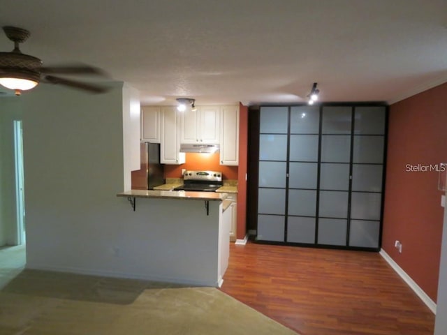 kitchen featuring a breakfast bar area, a peninsula, electric range, freestanding refrigerator, and under cabinet range hood