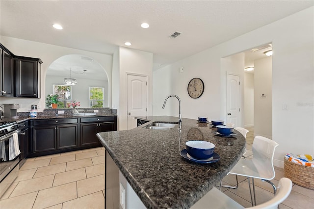 kitchen with sink, a breakfast bar area, dark stone countertops, a kitchen island with sink, and gas stove