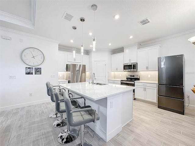 kitchen featuring appliances with stainless steel finishes, a center island with sink, pendant lighting, sink, and white cabinetry