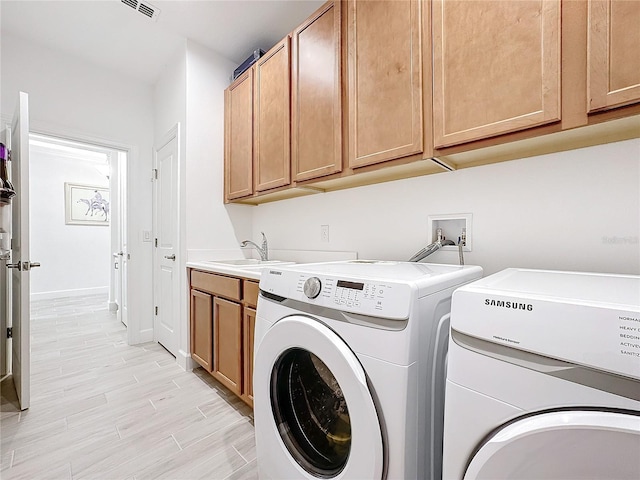 clothes washing area featuring sink, cabinets, washing machine and clothes dryer, and light hardwood / wood-style floors