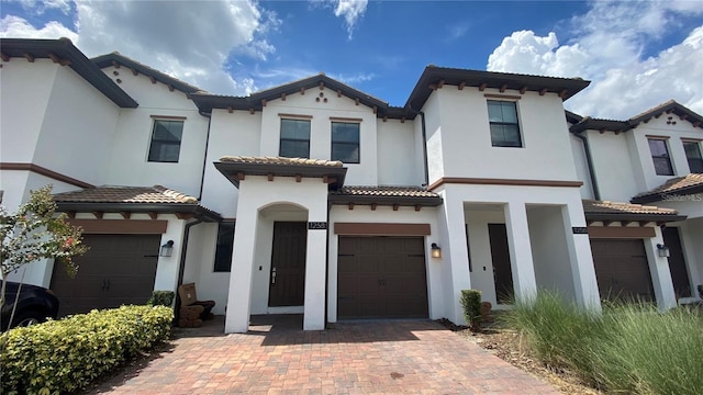 mediterranean / spanish home featuring a garage, a tiled roof, decorative driveway, and stucco siding