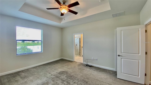 unfurnished bedroom with a tray ceiling, visible vents, light carpet, ensuite bath, and baseboards