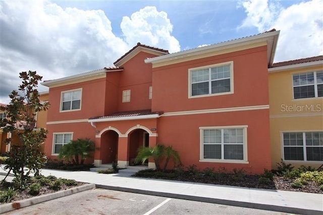 view of front of house with a tiled roof, uncovered parking, and stucco siding