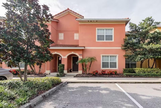 mediterranean / spanish-style home with a tiled roof, uncovered parking, and stucco siding