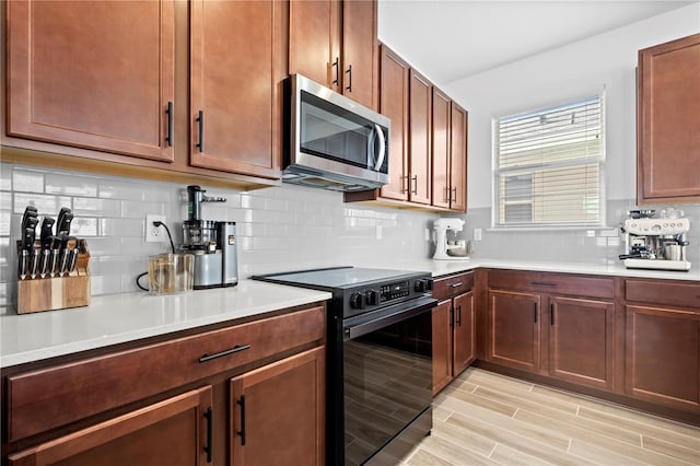 kitchen featuring black range with electric stovetop, stainless steel microwave, light countertops, decorative backsplash, and wood tiled floor