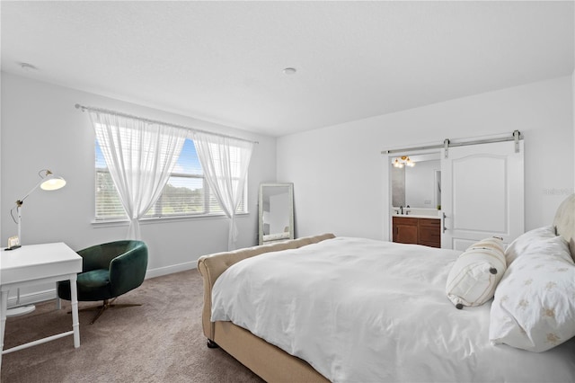 carpeted bedroom with ensuite bath, a barn door, and baseboards