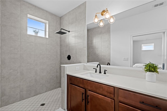 bathroom with visible vents, a healthy amount of sunlight, tiled shower, and vanity