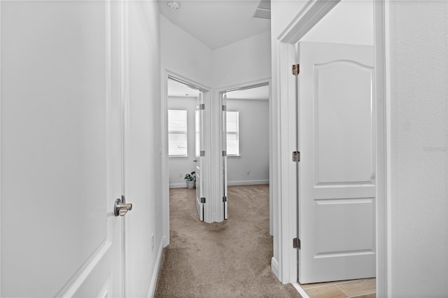 hallway featuring light carpet and baseboards