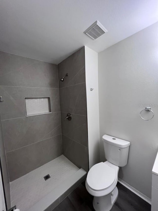 bathroom with a tile shower, hardwood / wood-style flooring, and toilet