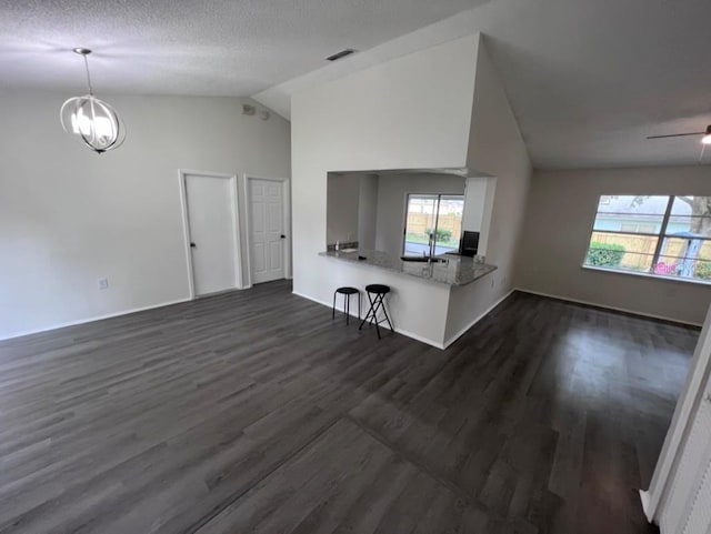 unfurnished living room featuring lofted ceiling, a healthy amount of sunlight, dark wood-type flooring, and a chandelier