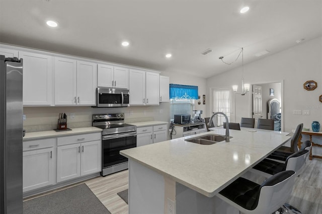 kitchen with a kitchen island with sink, stainless steel appliances, a sink, white cabinets, and decorative light fixtures