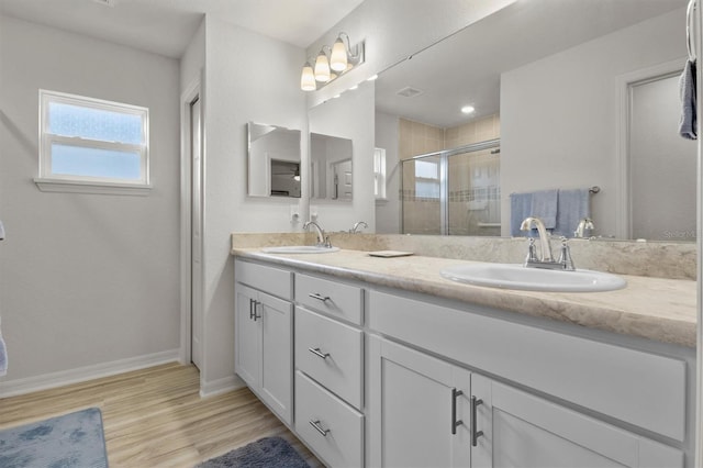 full bathroom featuring wood finished floors, a sink, a shower stall, and double vanity