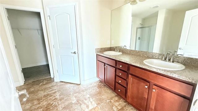 full bath with a walk in closet, a shower stall, double vanity, and a sink