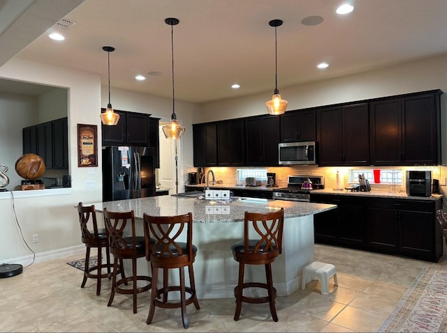 kitchen with stainless steel appliances, a kitchen island with sink, a sink, and light stone countertops