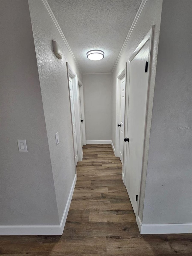 hall featuring baseboards, dark wood finished floors, a textured wall, a textured ceiling, and crown molding