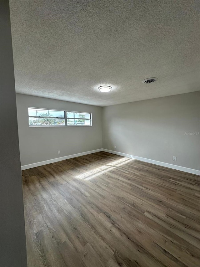 unfurnished room featuring a textured ceiling, dark wood finished floors, visible vents, and baseboards