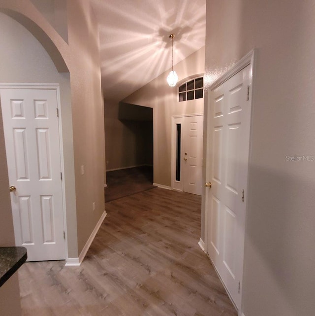 corridor featuring arched walkways, vaulted ceiling, baseboards, and wood finished floors