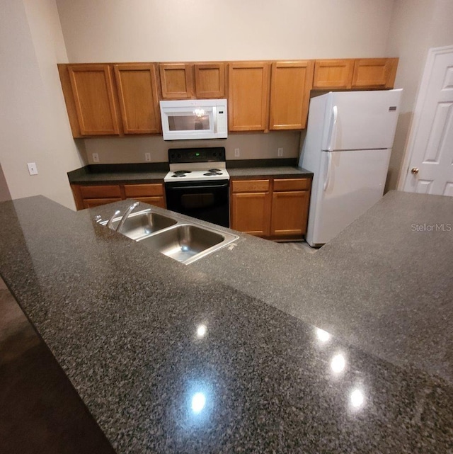 kitchen featuring white appliances, dark stone countertops, brown cabinets, and a sink