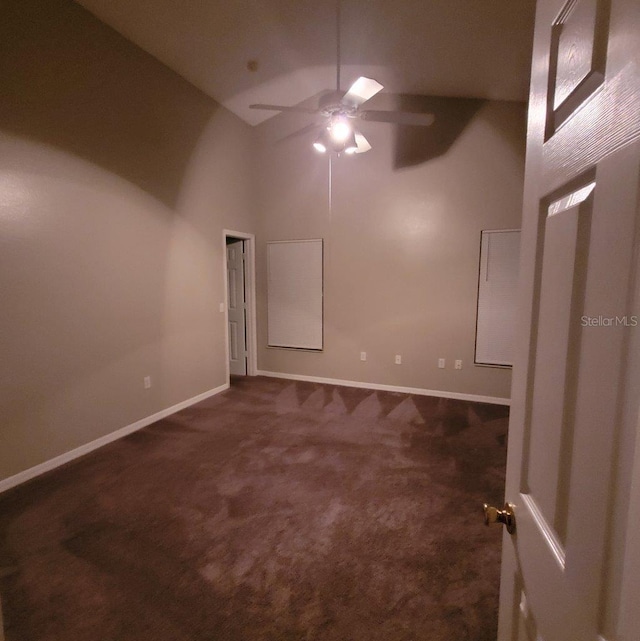 empty room featuring baseboards, high vaulted ceiling, dark colored carpet, and a ceiling fan