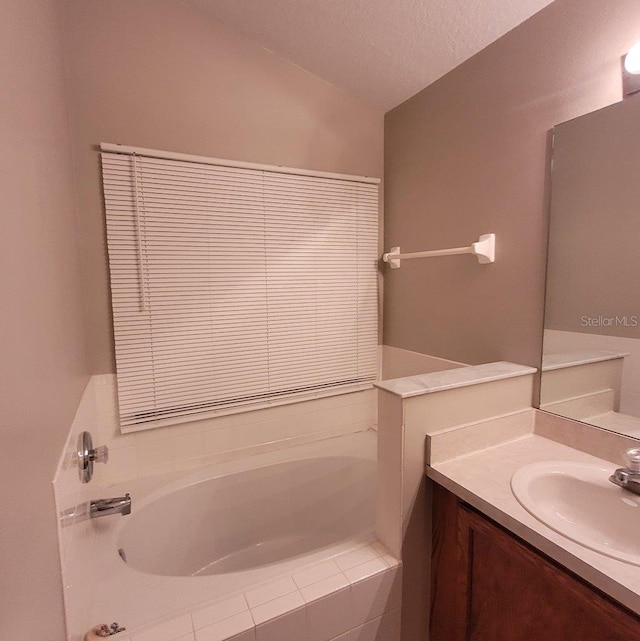 bathroom with a garden tub, vanity, and a textured ceiling