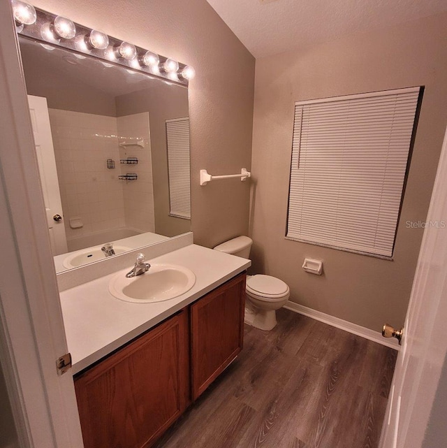 bathroom with toilet, wood finished floors, vanity, baseboards, and  shower combination