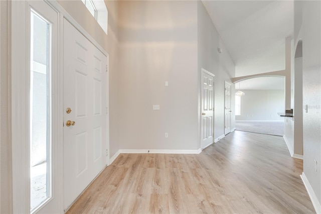 entrance foyer featuring arched walkways, a towering ceiling, baseboards, and light wood-type flooring