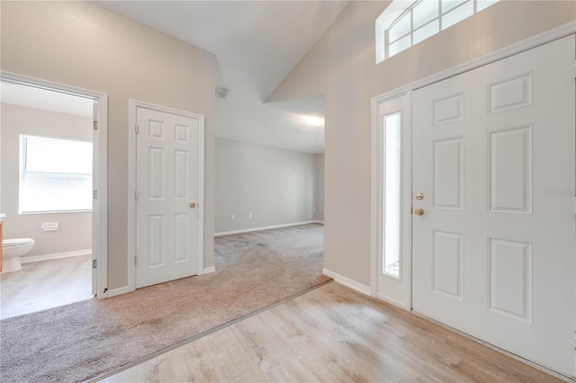 carpeted foyer with baseboards, visible vents, high vaulted ceiling, and wood finished floors