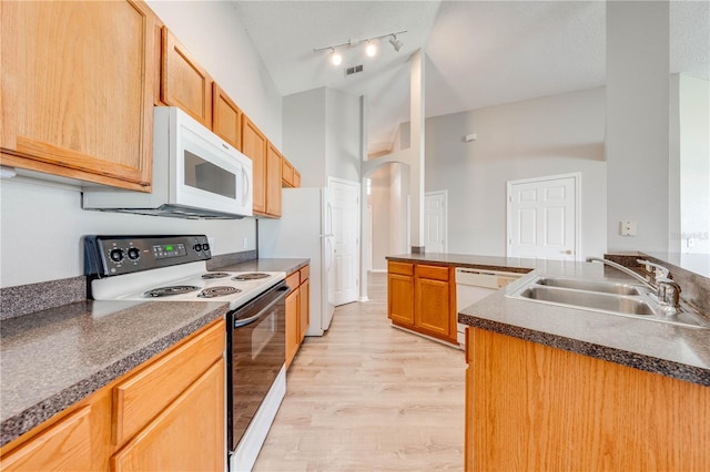kitchen featuring a sink, light wood-style flooring, white appliances, dark countertops, and arched walkways