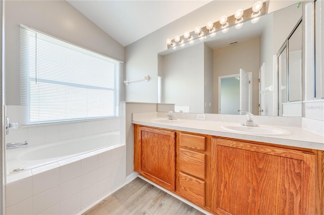 bathroom with double vanity, a bath, wood finished floors, and a sink