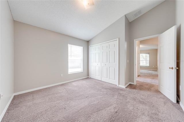 unfurnished bedroom with carpet floors, a textured ceiling, lofted ceiling, and visible vents