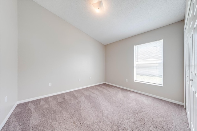 spare room with baseboards, lofted ceiling, carpet, and a textured ceiling