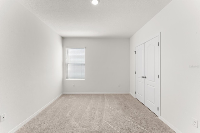 unfurnished bedroom featuring a textured ceiling, a closet, and light colored carpet