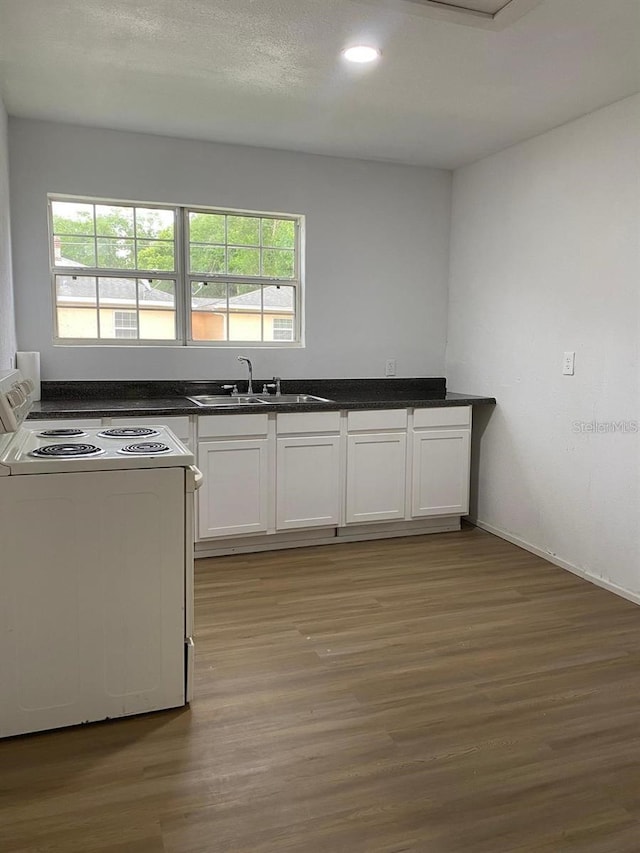 kitchen with white electric stove, dark countertops, a sink, white cabinetry, and a wealth of natural light