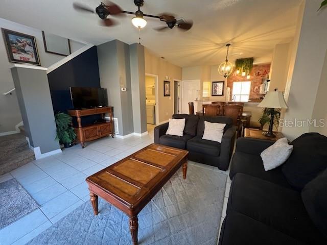 tiled living room with ceiling fan with notable chandelier