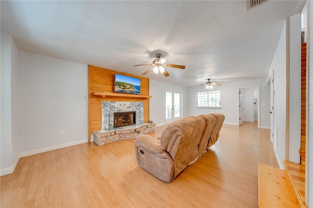 living room featuring a stone fireplace, light hardwood / wood-style flooring, and a textured ceiling