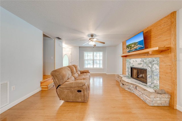 living room with ceiling fan, a textured ceiling, a fireplace, and light hardwood / wood-style flooring