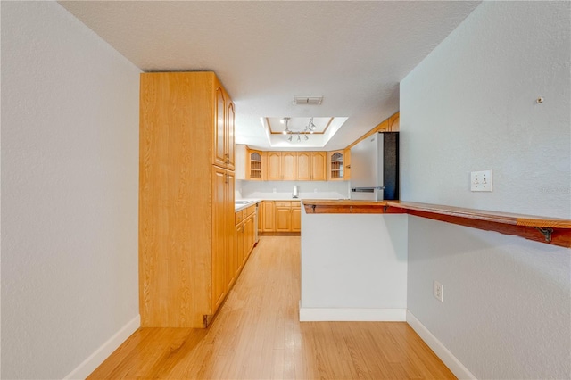 kitchen featuring light hardwood / wood-style flooring, stainless steel refrigerator, a skylight, light brown cabinetry, and a raised ceiling