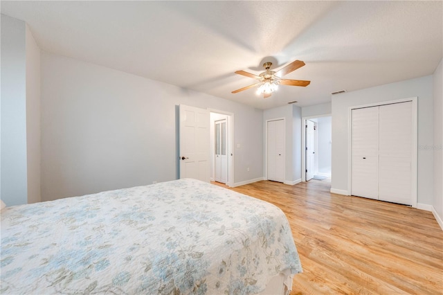 bedroom with ceiling fan, two closets, and light hardwood / wood-style floors