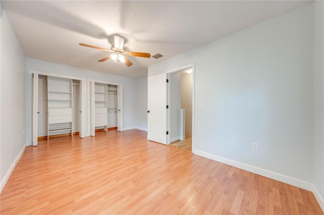 unfurnished bedroom featuring multiple closets, ceiling fan, a textured ceiling, and light wood-type flooring