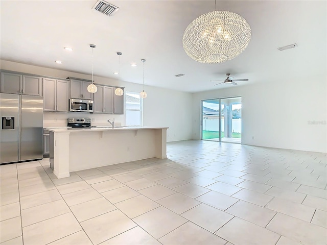 kitchen featuring gray cabinets, appliances with stainless steel finishes, a kitchen island with sink, and hanging light fixtures