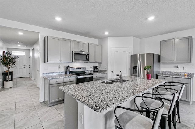 kitchen with sink, a breakfast bar area, a kitchen island with sink, stainless steel appliances, and light stone countertops