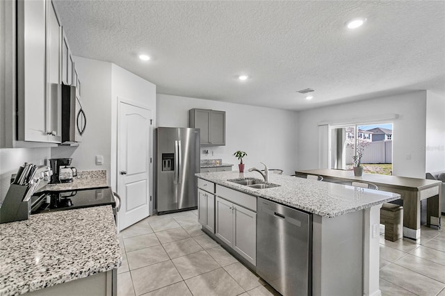 kitchen featuring sink, gray cabinetry, a kitchen island with sink, stainless steel appliances, and light stone countertops