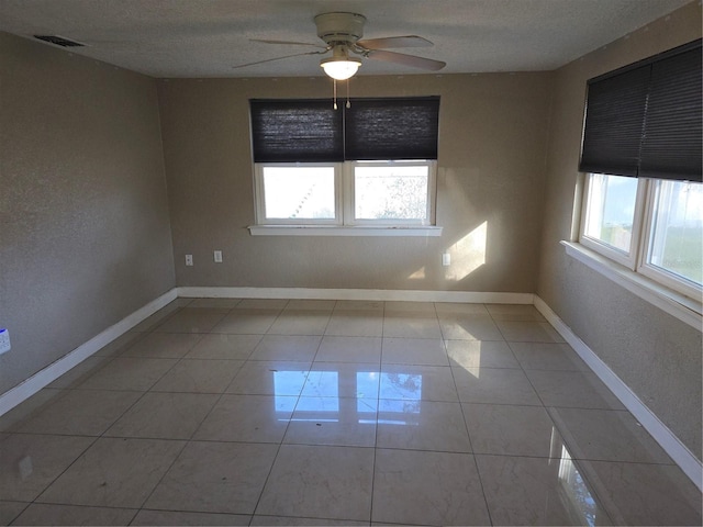 tiled spare room with ceiling fan, plenty of natural light, and a textured ceiling