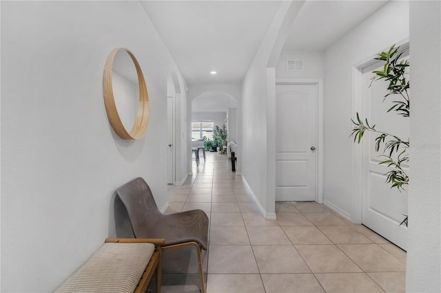 corridor featuring arched walkways, visible vents, baseboards, and light tile patterned flooring