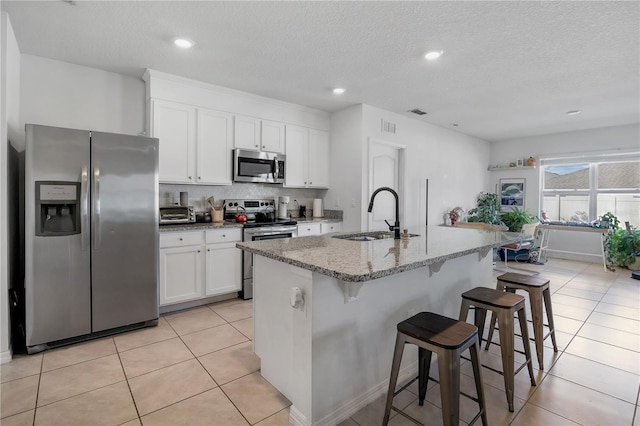 kitchen with stainless steel appliances, a kitchen island with sink, a sink, white cabinetry, and a kitchen bar