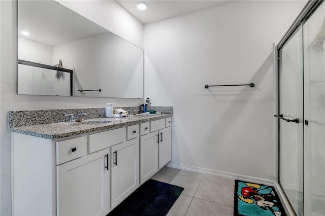 bathroom featuring double vanity, a shower with shower door, a sink, tile patterned flooring, and baseboards