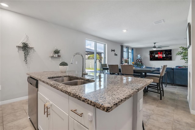 kitchen featuring an island with sink, light stone countertops, stainless steel dishwasher, sink, and white cabinetry